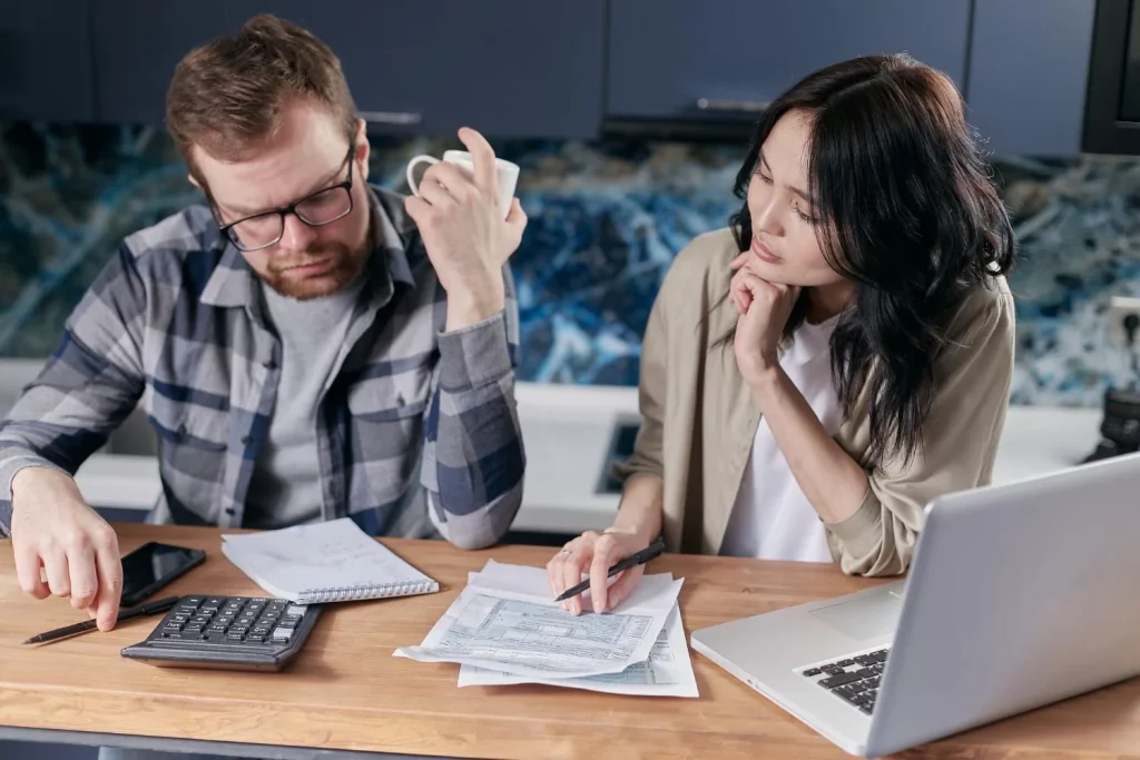Two colleagues engaged in a work discussion around an office table, using a calculator and documents.