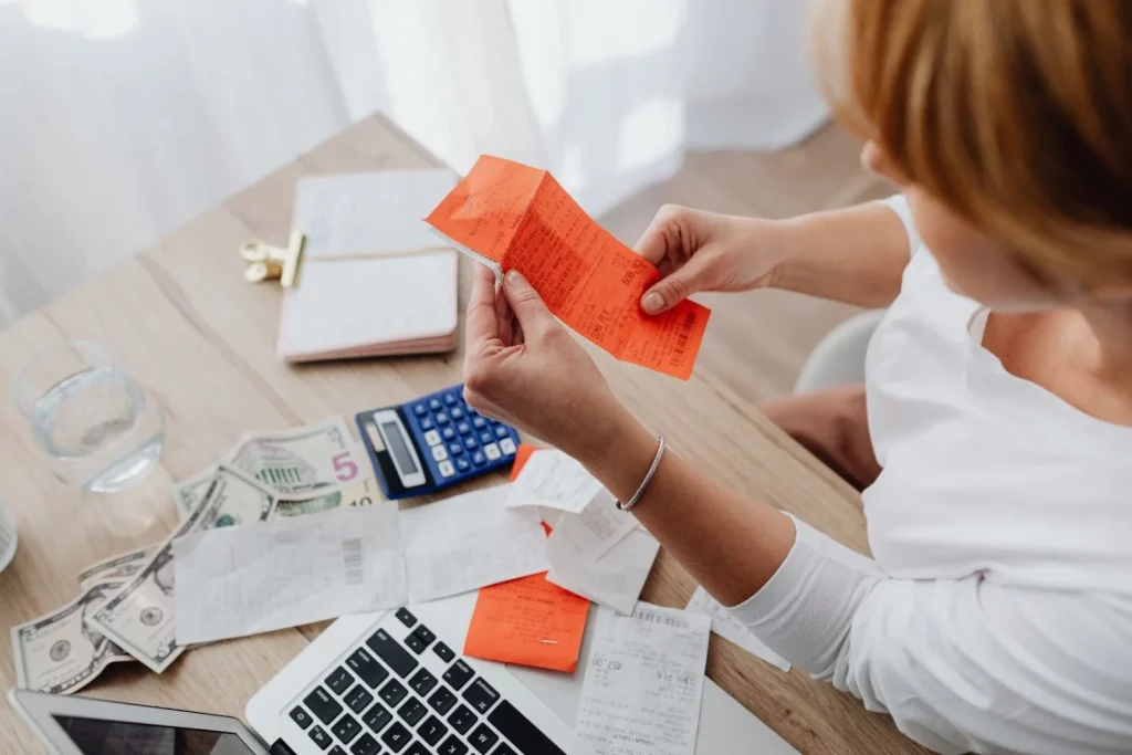 Top view of a woman managing finances on a laptop surrounded by receipts and calculator.