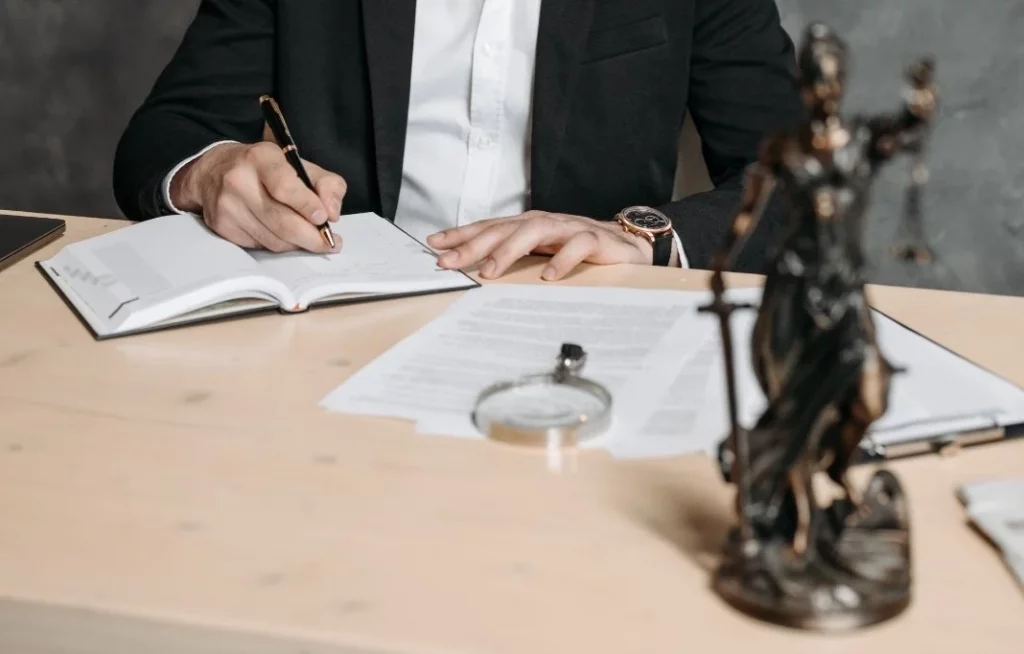 Professional lawyer in a suit taking notes at a desk with legal documents and statue.